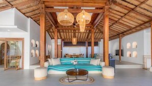 A spacious living area with a high ceiling, wooden beams, and a central seating area with a sofa and ottoman. - Villa Elora Canggu (Bali)