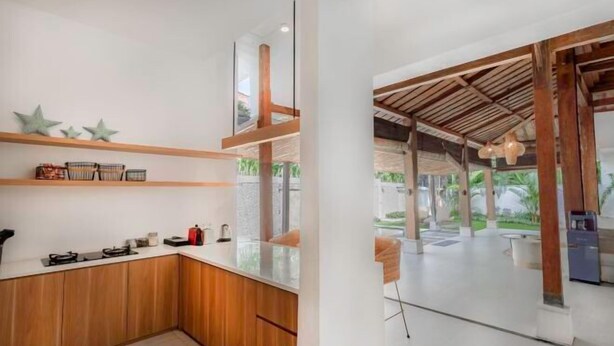 A modern kitchen with wooden cabinets, a countertop, and a view of an outdoor patio area. - Villa Elora Canggu (Bali)