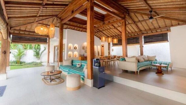 A spacious indoor area with a thatched roof, a sofa set, a dining area, and a view of greenery outside. - Villa Elora Canggu (Bali)