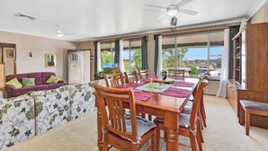 A dining area with a wooden table and chairs, a purple sofa, and a view of the outdoors through large windows.