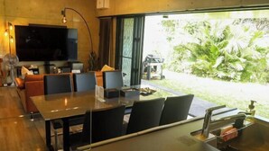 Ein modernes Wohnzimmer mit Flachbildfernseher, einem Essbereich mit Glastisch und Blick auf einen Garten.