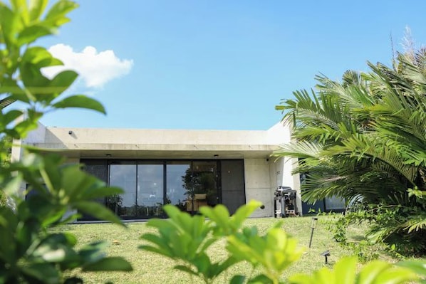A modern building with large windows, a flat roof, and a well-maintained lawn with palm trees.