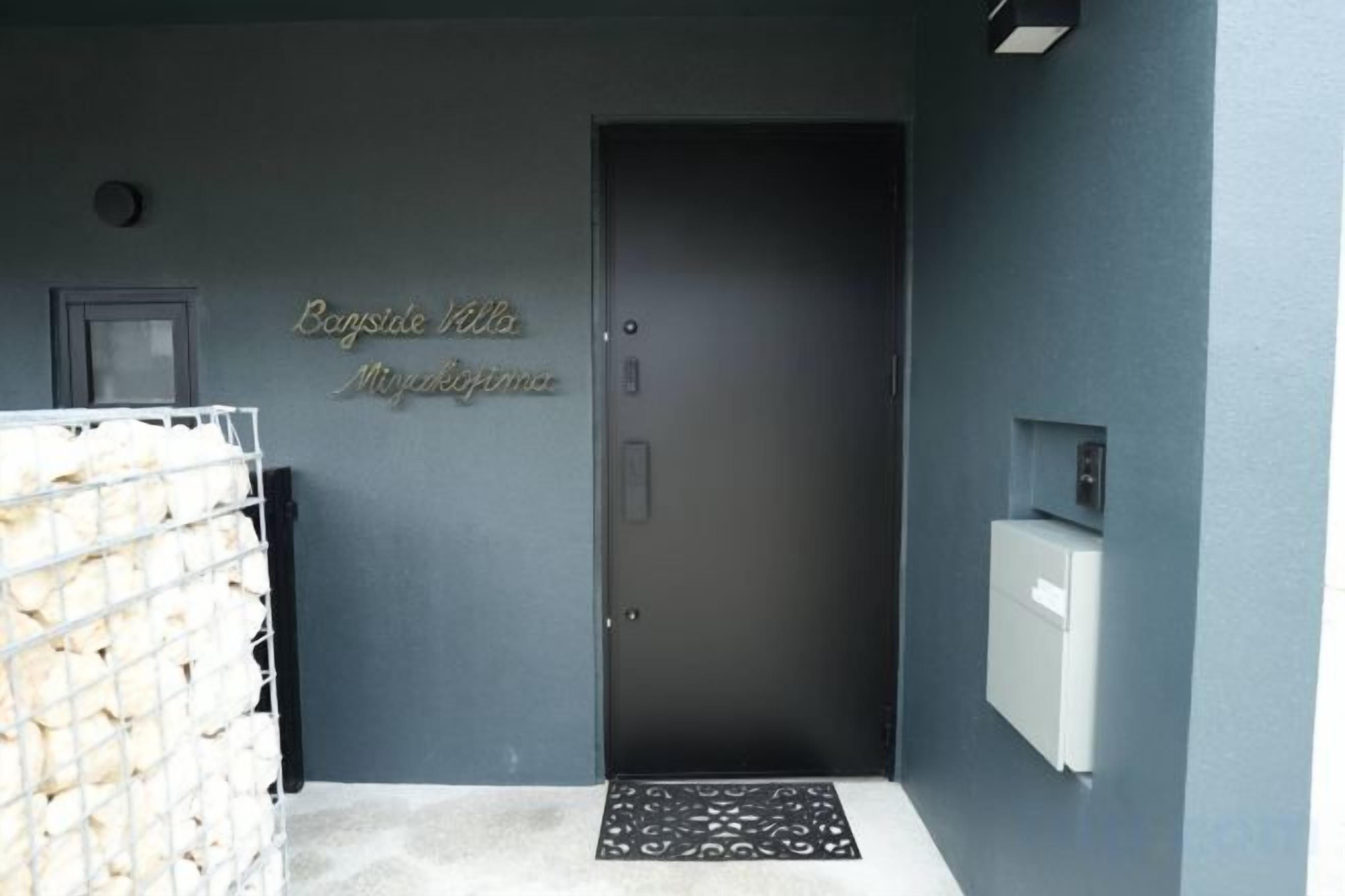Hotellin sisäänkäynti, jossa on tumma ovi, vastaanottoalue ja pieni jääkaappi.