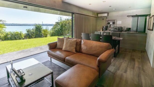 Ein modernes Wohnzimmer mit Ledersofa, Essbereich und Blick auf ein Gewässer.