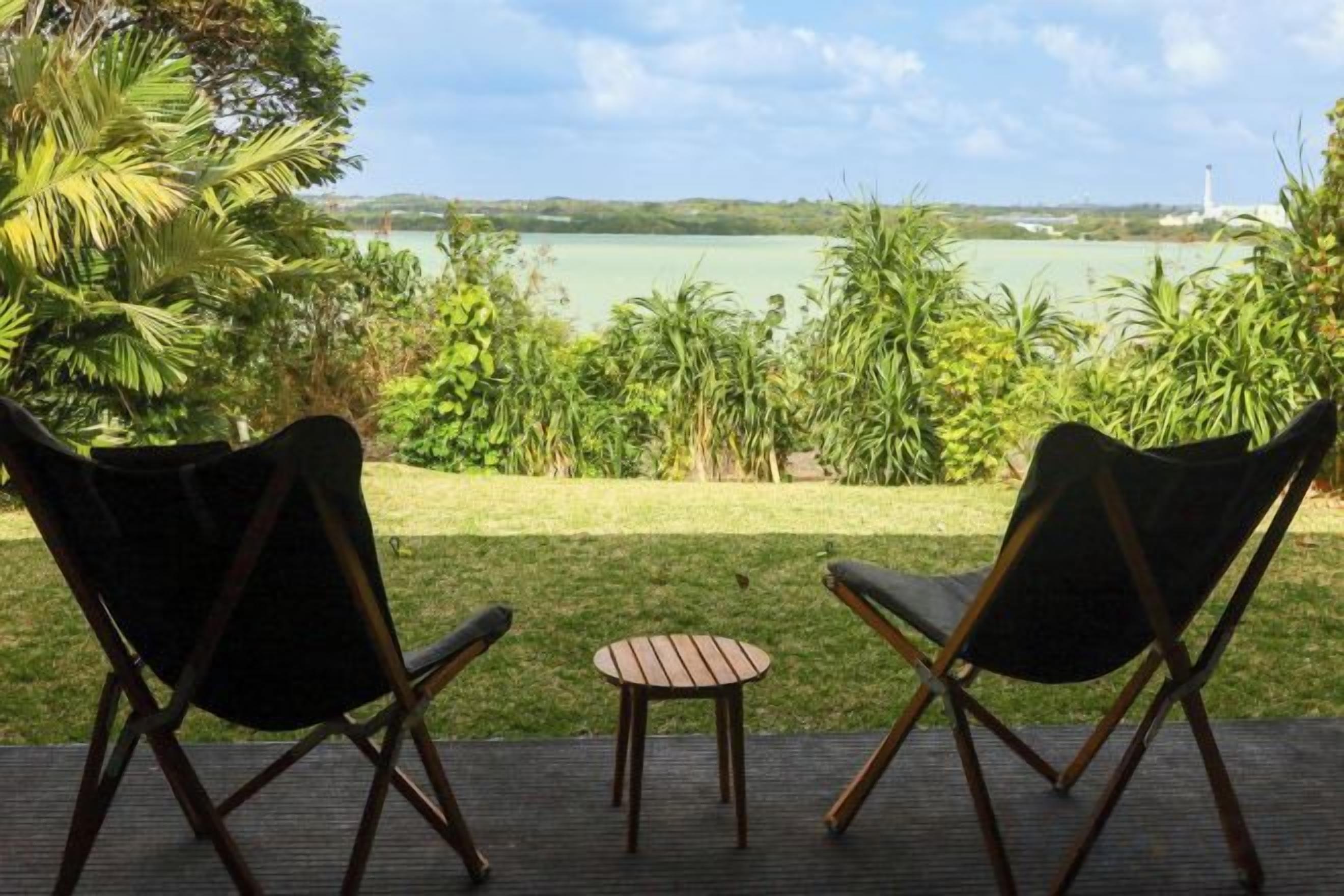 Two chairs and a small table on a deck with a view of a lake and greenery.