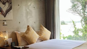 Ein Hotelzimmer mit einem Bett, Kissen, einem Nachttisch, einer Lampe und Blick auf Grün.