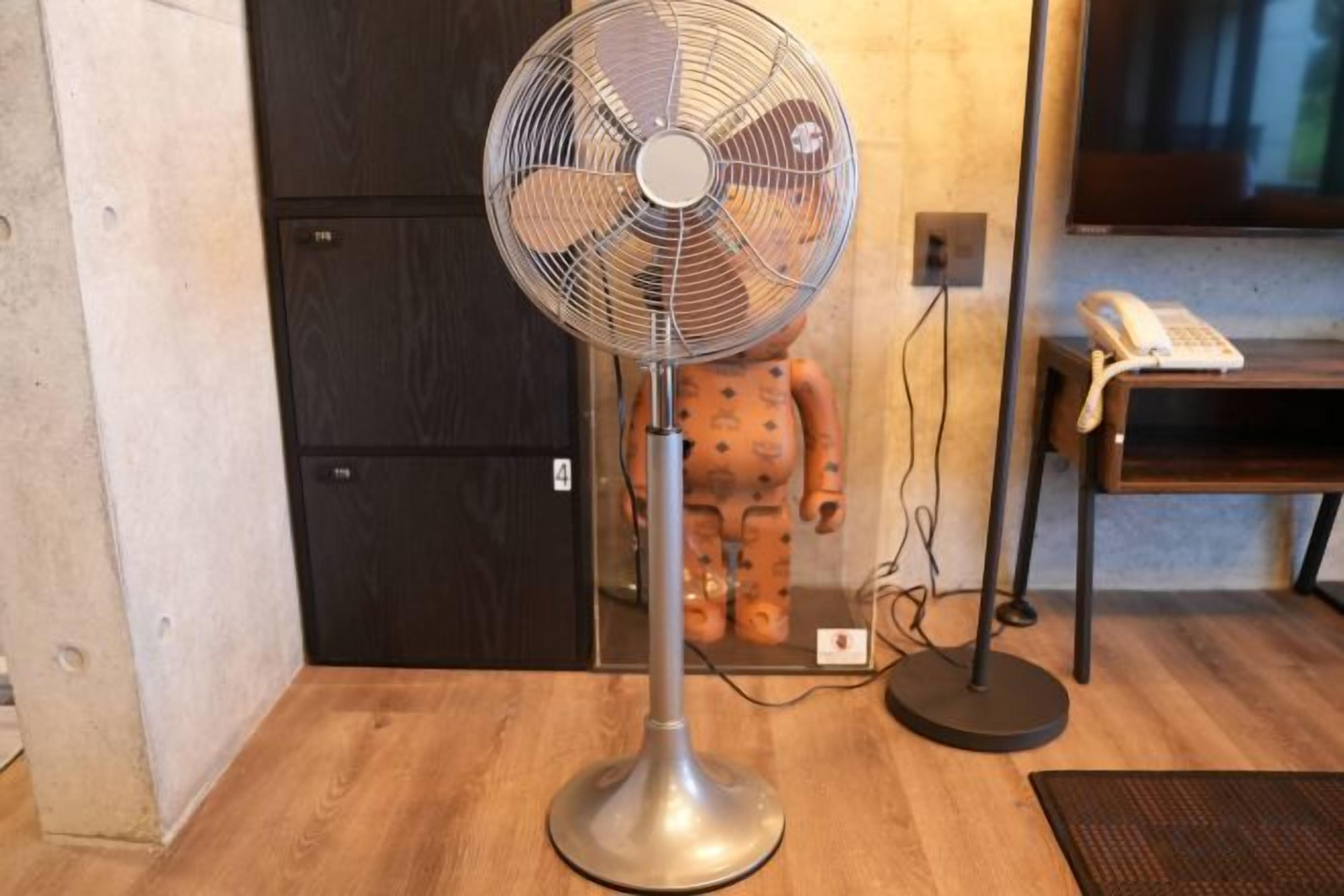 A standing fan, a telephone, and a wooden floor in a room.