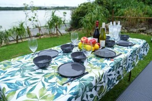An outdoor dining table set with black plates, bowls, and glasses, a bottle of wine, and a fruit bowl.