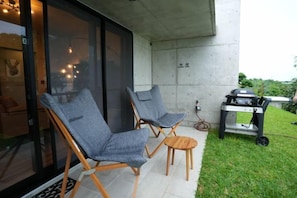 Une terrasse avec deux fauteuils gris rembourrés, une petite table ronde et un barbecue.