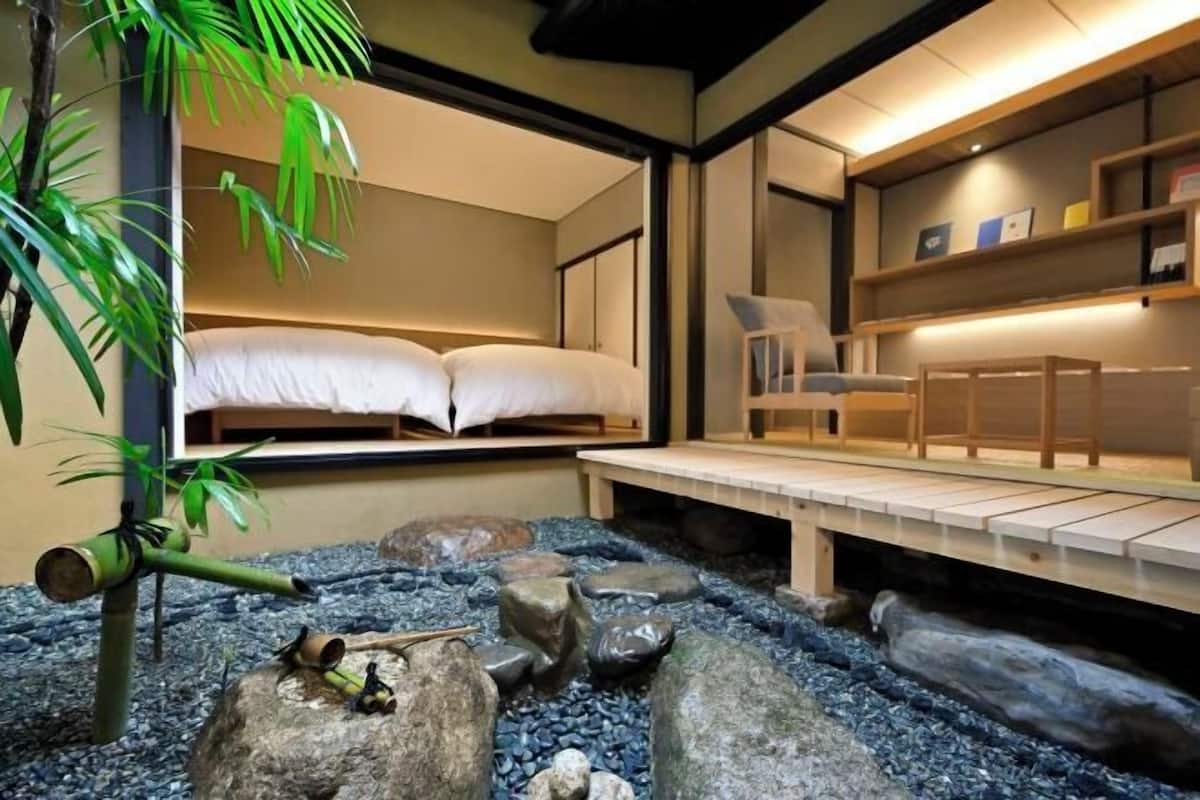 A room with a bed, a desk, and a small indoor garden with rocks and plants.