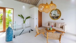 A modern living room with a sofa, two chairs, a coffee table, and a hanging light fixture. - Villa Maria by Pertama Stay (Bali)