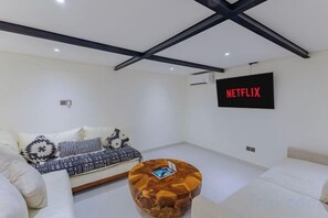 A modern living room with a sofa, a coffee table, and a wall-mounted TV displaying 'NETFLIX'. - Villa Maria by Pertama Stay (Bali)