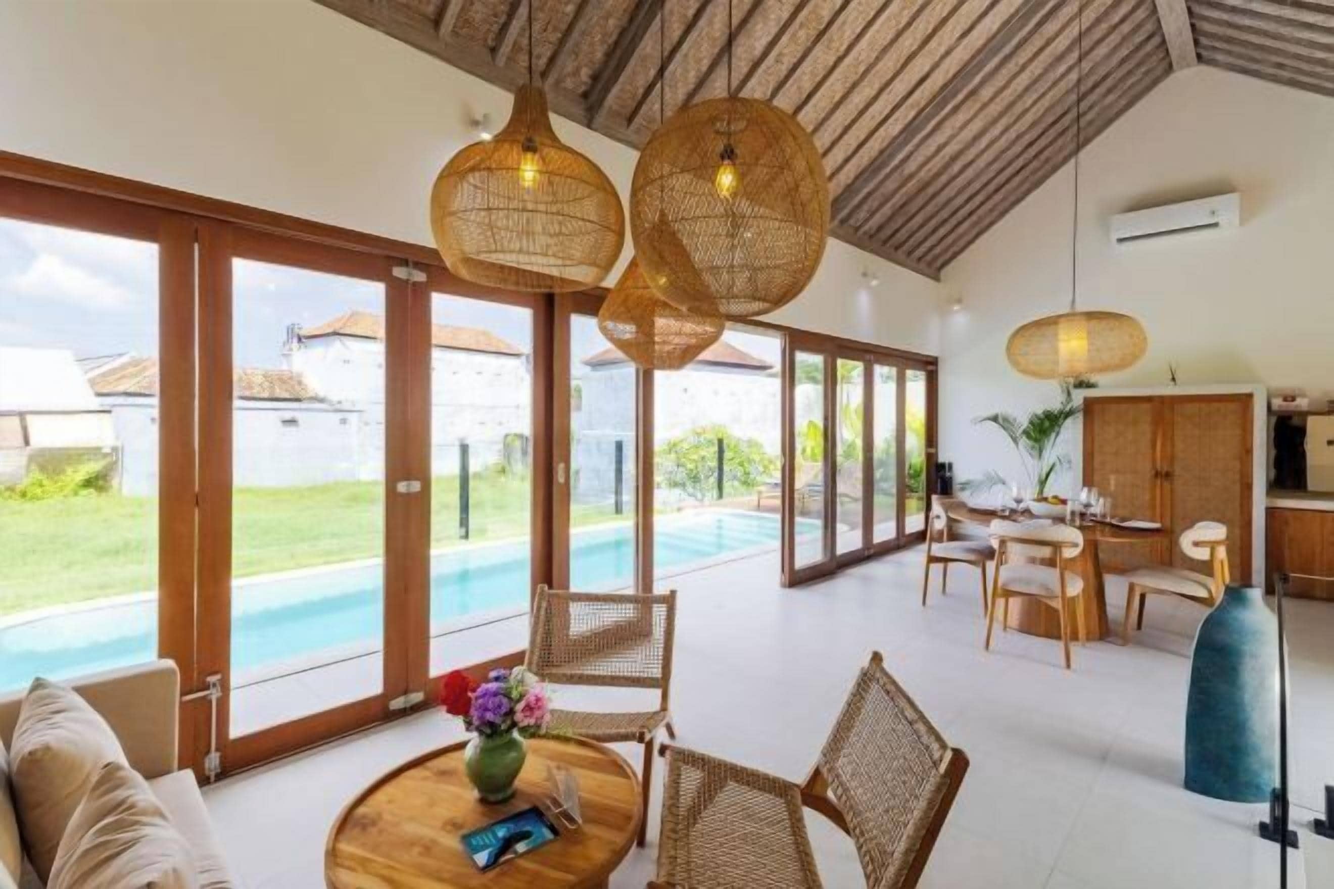A spacious living area with a pool, wicker furniture, and large windows.