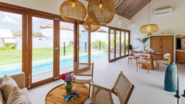 A spacious living area with a pool, wicker furniture, and large windows. - Villa Maria by Pertama Stay (Bali)