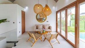 A modern interior with a glass door leading to a pool, a round table with chairs, and a ceiling with exposed beams. - Villa Maria by Pertama Stay (Bali)