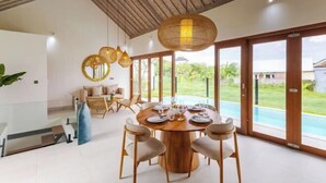 A dining area with a round wooden table, chairs, and hanging lights. - Villa Maria by Pertama Stay (Bali)