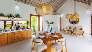 A modern kitchen with wooden cabinets, a dining area with a round table, and a living space with a sofa and chairs. - Villa Maria by Pertama Stay (Bali)