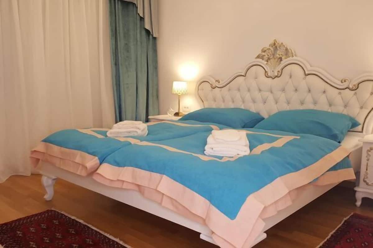 A neatly made bed with a blue and peach bedspread, a white headboard, and a bedside lamp.