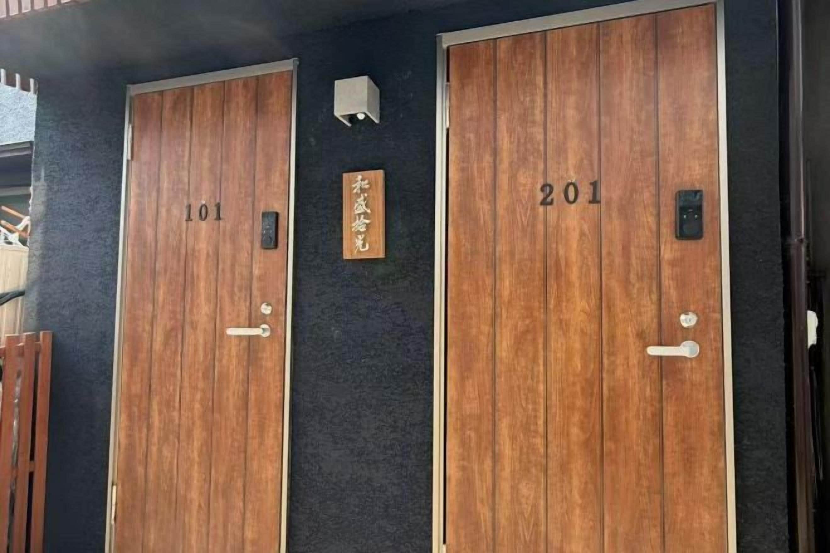 Two wooden doors with numbers 101 and 201, a small sign with Japanese characters, and a light fixture above the doors.