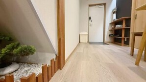 A hallway with a wooden floor, a small potted plant, and a door with a green exit sign. - He Sheng Shi Guang101 (Osaka)