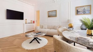 Un saló modern amb un sofà blanc, una taula de centre rodona i una taula de menjador amb cadirees. Hi ha una televisió de pantalla plana penjada a la paret i un quadre sobre el sofà.