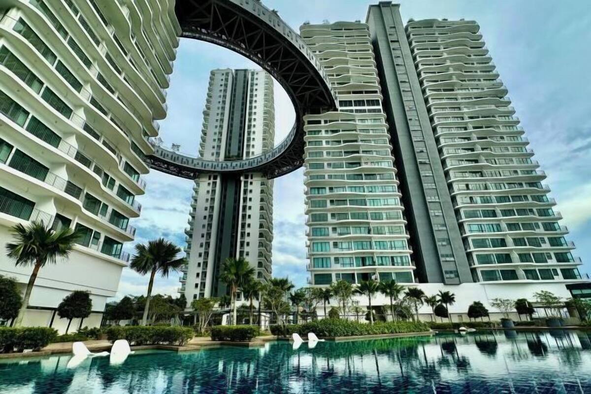 Un hôtel de grande hauteur doté d’une structure en forme de pont incurvé remarquable, d’une piscine et de palmiers.
