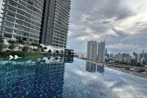 Un hotel modern amb una piscina d'infinity al terrat, edificis alts i un cel nuvolós.