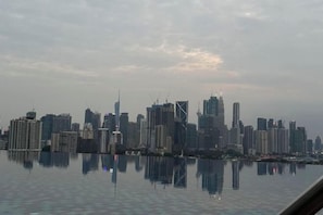 Le profil d’une ville se reflète sur une étendue d’eau calme, avec divers gratte-ciel et des grues de construction.