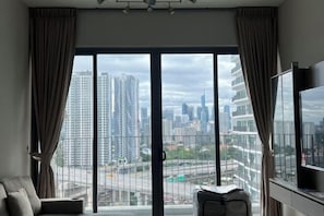 Une chambre d’hôtel moderne avec une grande fenêtre, un canapé, une télévision et une petite table.