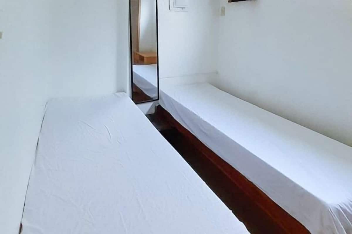 A single bed with a wooden headboard, a white wall, and a mirror reflecting part of the room.