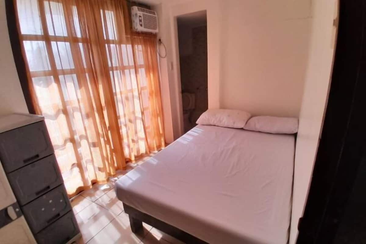 A bedroom with a bed, a dresser, and a window with curtains.
