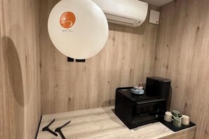 A room with a wooden wall, a white air conditioning unit, a black coffee machine, and a small table with cups and a decorative item. - WATEL ASAKUSA (Tokyo)