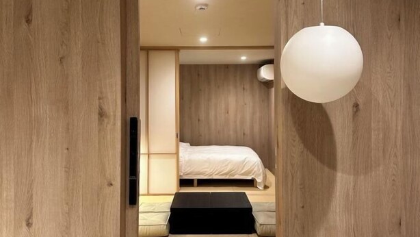 A modern bedroom with a wooden floor, a bed with white bedding, a black bedside table, and a hanging light fixture. - WATEL ASAKUSA (Tokyo)