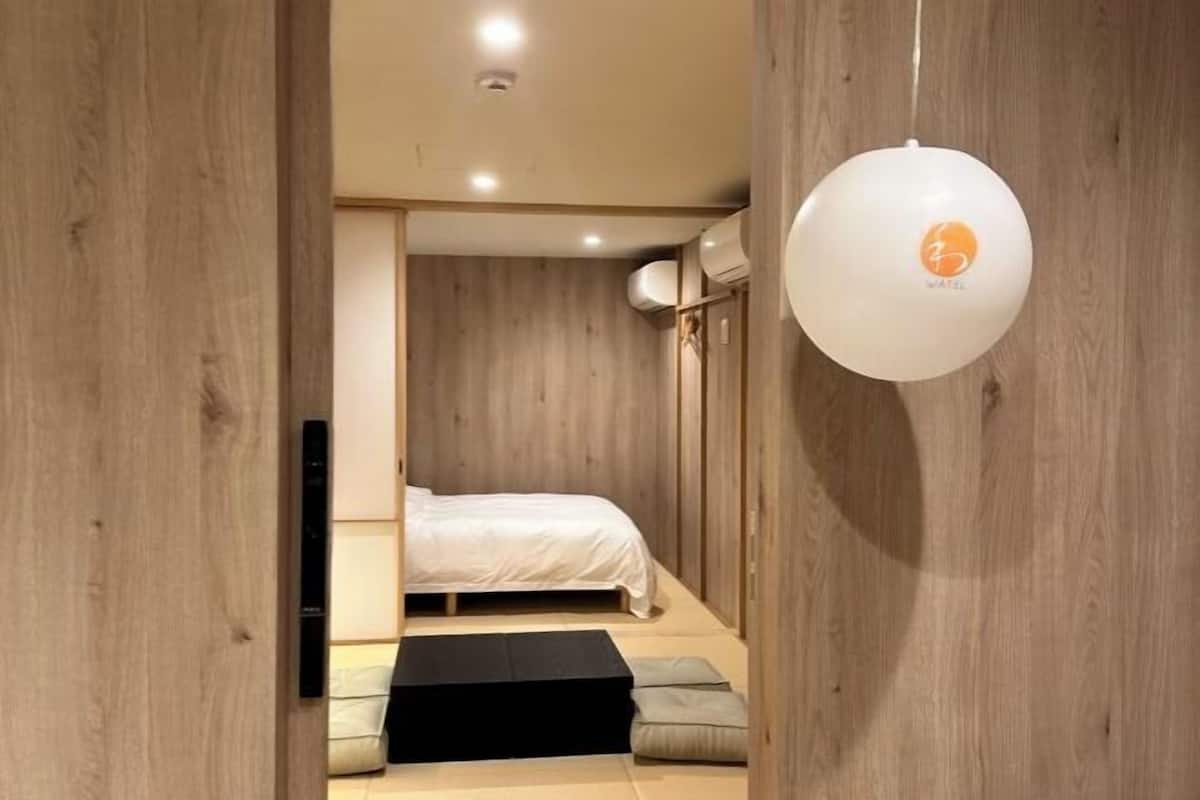 A minimalist bedroom with a bed, a black platform, and a white wall-mounted light fixture.