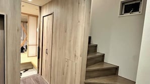 A hallway with wooden panel walls, a set of wooden stairs, and a small window with a picture frame. - WATEL ASAKUSA (Tokyo)