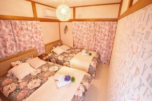 A room with two beds, floral curtains, a hanging light fixture, and a wall with alphabet patterns.