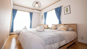 A bedroom with a wooden bed, blue curtains, a hanging light fixture, and a framed picture on the wall. - Sakura Retreat (Tokyo)