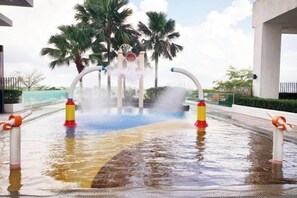Un élément décoratif aquatique comprenant une fontaine et des palmiers, intégré dans un espace paysager.