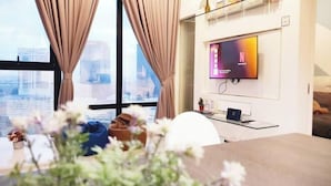A modern living room with a large window, a flat-screen TV mounted on the wall, and a dining area with a table and chairs. - Delight Homestay Mosaic Southkey (Plentong)