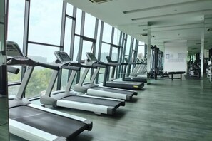Une salle de sport avec des tapis de course alignés le long d’un mur, face à de grandes fenêtres.