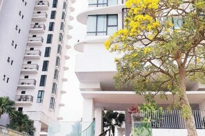 Un immeuble à plusieurs étages, doté de balcons, et un arbre aux fleurs jaunes.