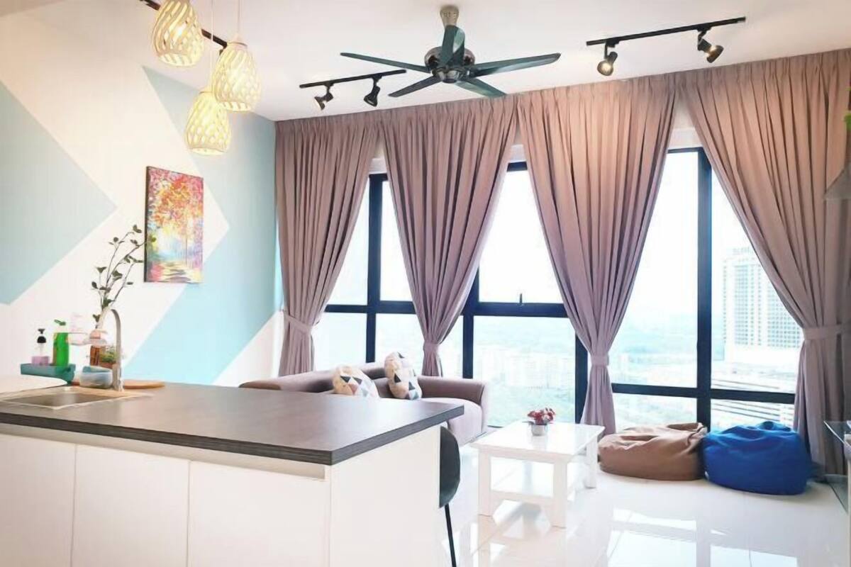 Un espacio habitable moderno con una isla de cocina, ventilador de techo, ventanas amplias con cortinas y vistas a la ciudad.