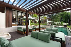 Ett modernt utomhusområde med loungekänsla, en pool, gröna, vadderade sittplatser och en pergola.