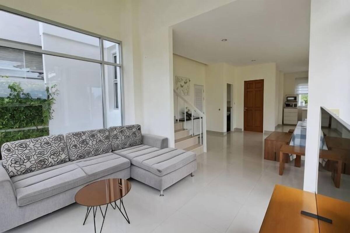 A modern living room with a sectional sofa, a small round table, and a dining area with a wooden table and chairs.