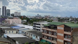 A cityscape with various buildings, including a prominent red building with balconies and a green roof. - Rattanakorn Mansion (Bangkok)
