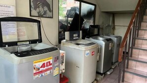 A room with a refrigerator, a washing machine, and a microwave. There is a window with a view of the outside, and a staircase is visible to the right. - Rattanakorn Mansion (Bangkok)