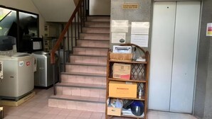 A staircase leading to an elevator, with a vending machine and a shelf with boxes and items on the left. - Rattanakorn Mansion (Bangkok)
