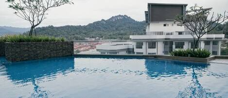 A swimming pool with a view of a modern building and mountains in the background.