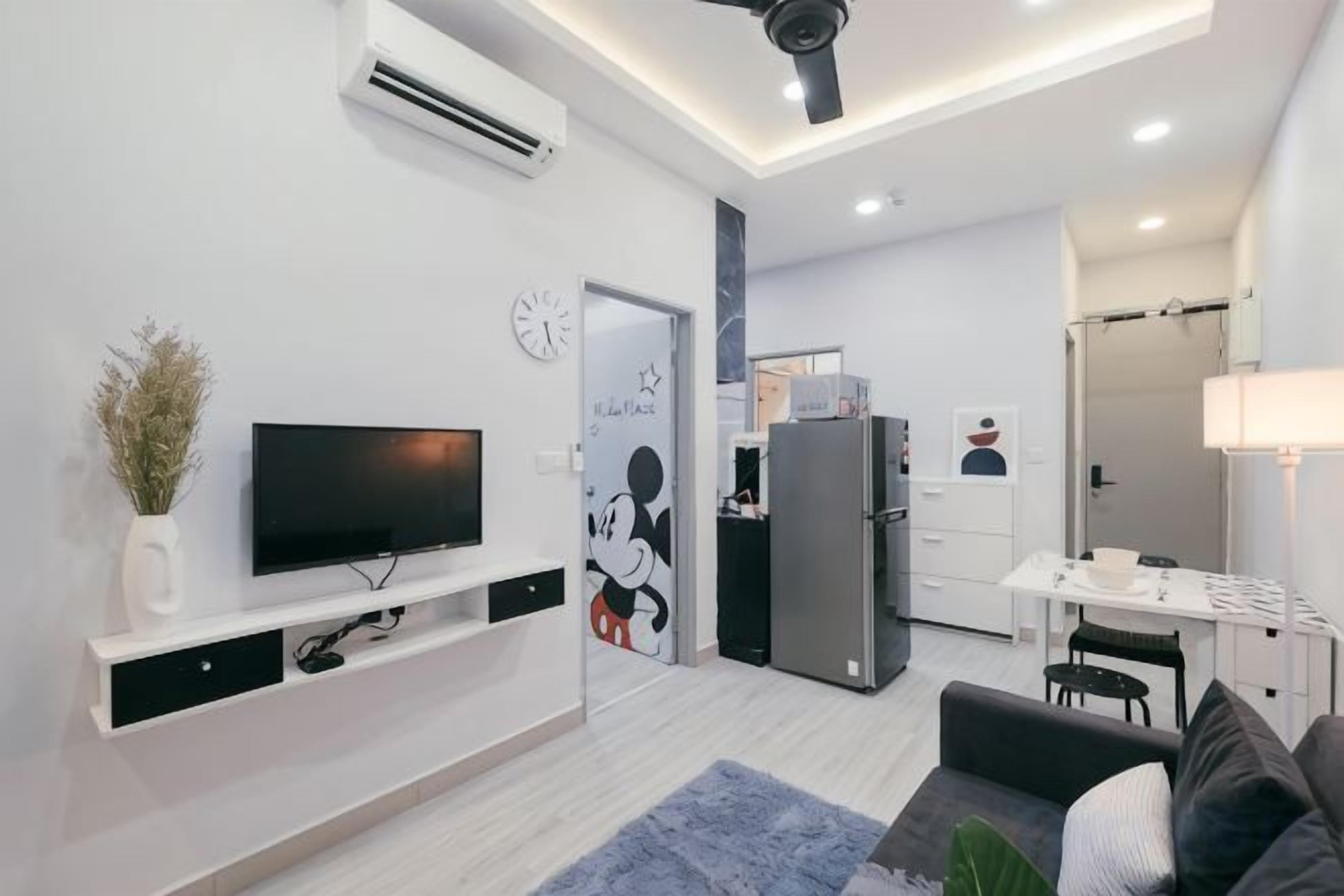 Un salon moderne avec un téléviseur à écran plat, une table basse et un canapé. Il y a également un coin cuisine équipé d’un réfrigérateur et d’une table à manger.