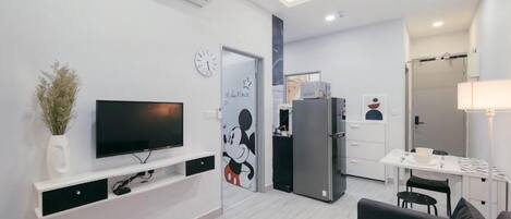 Ett modernt vardagsrum med en platt-TV, ett soffbord och en soffa. Det finns också ett köksområde med ett kylskåp och ett matbord.